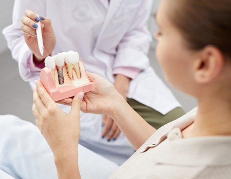 A dentist pointing to a dental implant model while talking with their patient