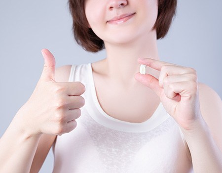 A happy woman holding her extracted tooth and giving a thumbs up 