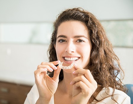 Woman smiling while holding clear aligner