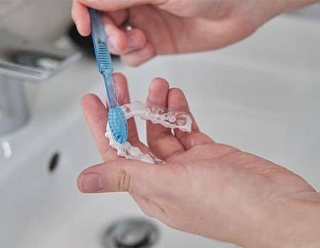 Patient cleaning clear aligner with toothbrush in sink