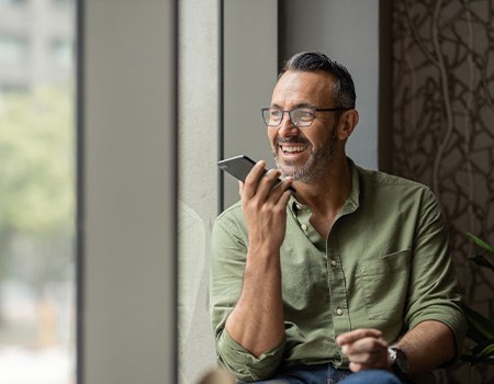 Man smiling while talking on speaker phone