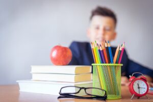 Books, apple, and school supplies in front of young boy