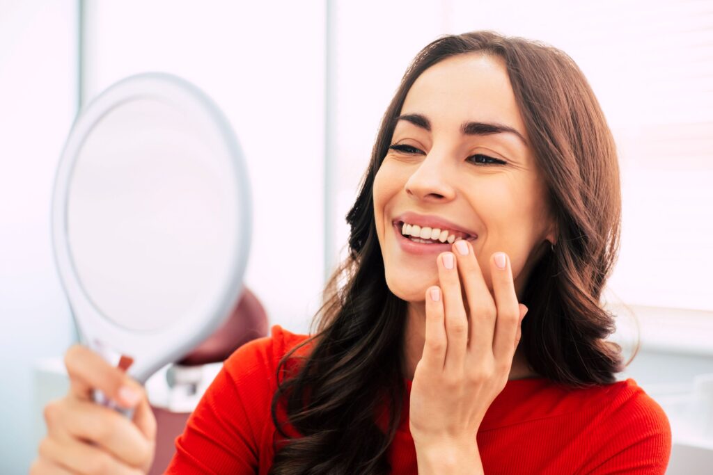 Woman in red shirt smiling at reflection in handheld mirror